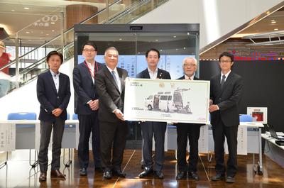 写真:福祉車両の写真がプリントされたプレートを掲げる関係者たち