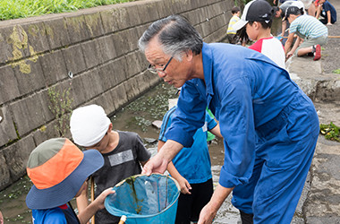 写真:用水を清掃する天野 武雄さんと子供たち