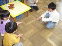 5歳児らいおん組が3歳児こあら組にコマを教えている写真