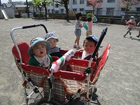 0歳児がワゴン車に乗って園庭散歩をしています。