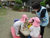 2歳児クラスが園庭でおままごとをしている写真です。