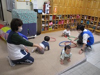 0歳が玄関ホールでフープで遊んでいる写真です。