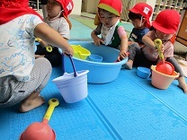 タライで水遊びをする1歳児の写真