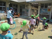 シャワーで水をかけてもらいながら遊ぶ子どもの写真