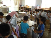 地震発生の放送に防災頭巾を被る子どもの写真