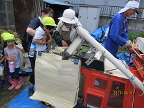 脱穀機を見学させてもらう子どもの写真