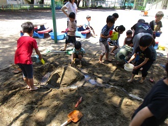 写真：5歳児が砂場に水路を作り、水を流して遊んでいる様子