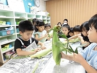 写真:とうもろこしの皮むきを見ている3歳児