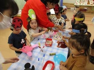 2歳児が5歳児のお店屋さんでうちわを作っている様子の写真