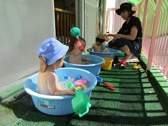 0歳児がテラスでタライに入って水遊びをしている様子の写真