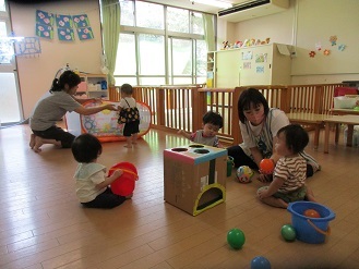 0歳児が保育室で保育者と一緒に遊んでいる様子の写真