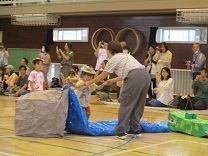 お母さんに手を添えてもらって川を飛び越える2歳児の写真