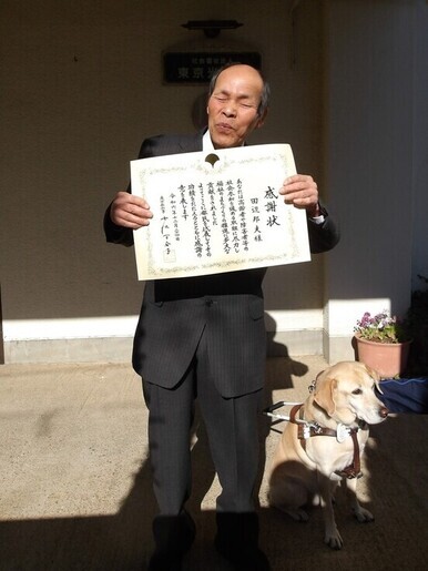 都知事感謝状を持つ田辺邦夫さんと、アイメイト(盲導犬)のデミータ
