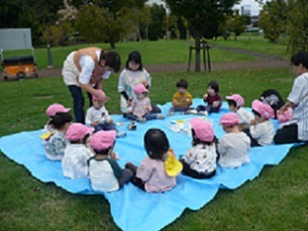 1歳児りす組がブルーシートの上でおやつを食べている様子の写真
