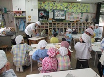 調理員からピザ作りの説明を受ける子どもの写真