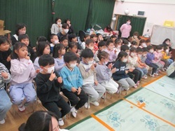 観劇会で歌を聴き、絵本のスライドショーを見る4・5歳児の画像
