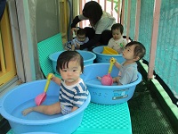 タライの中でおもちゃを持っている0歳児の様子の写真